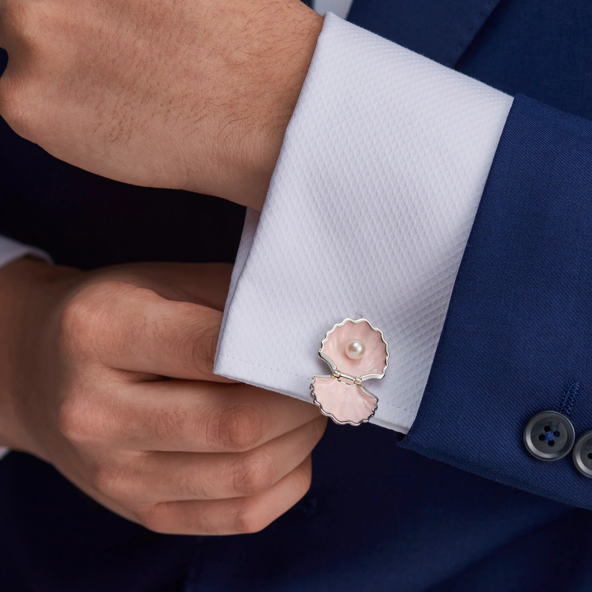 Cufflink with a pearl design on a white cuff against a blue suit background