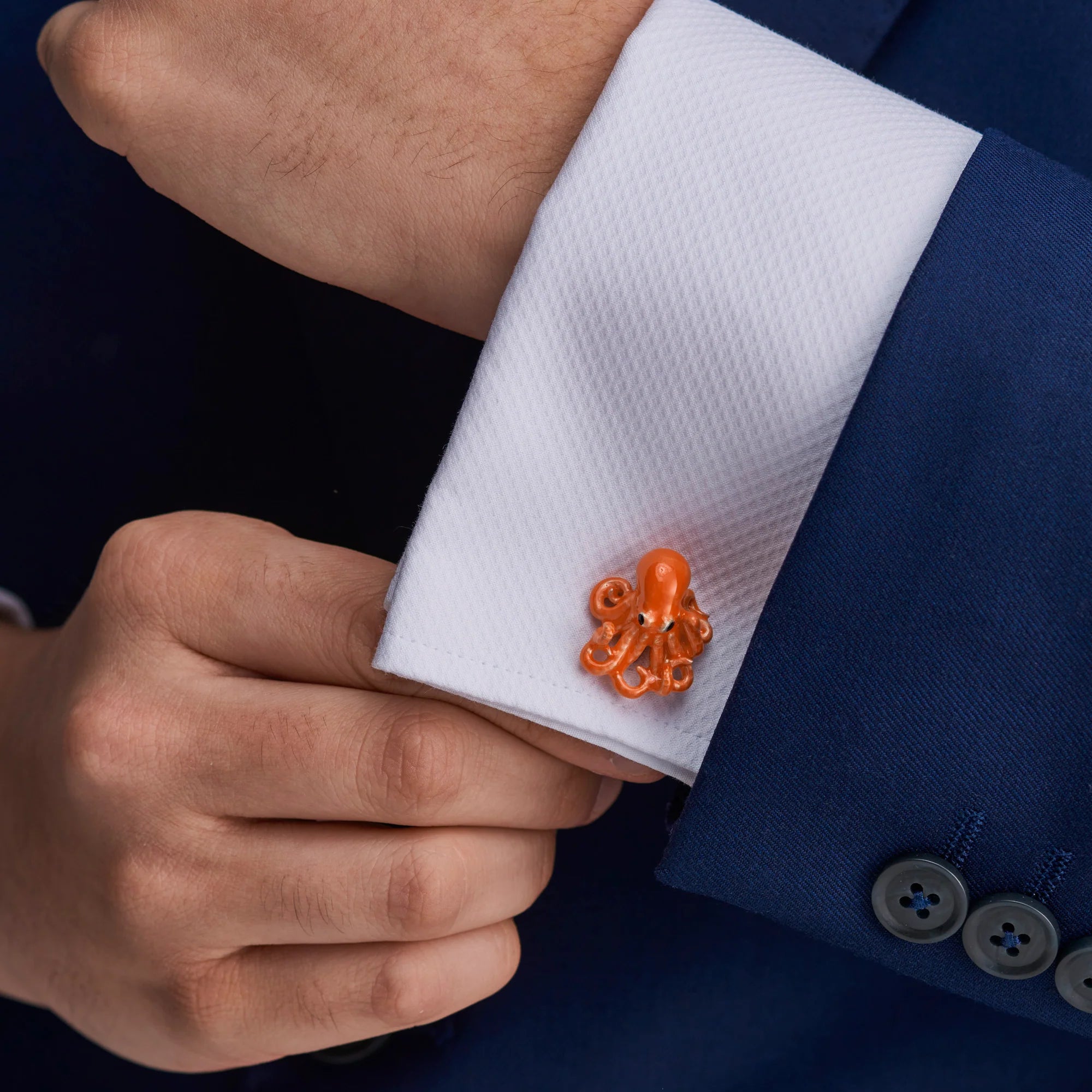 Orange octopus-shaped cufflink on a white shirt cuff with a blue suit.